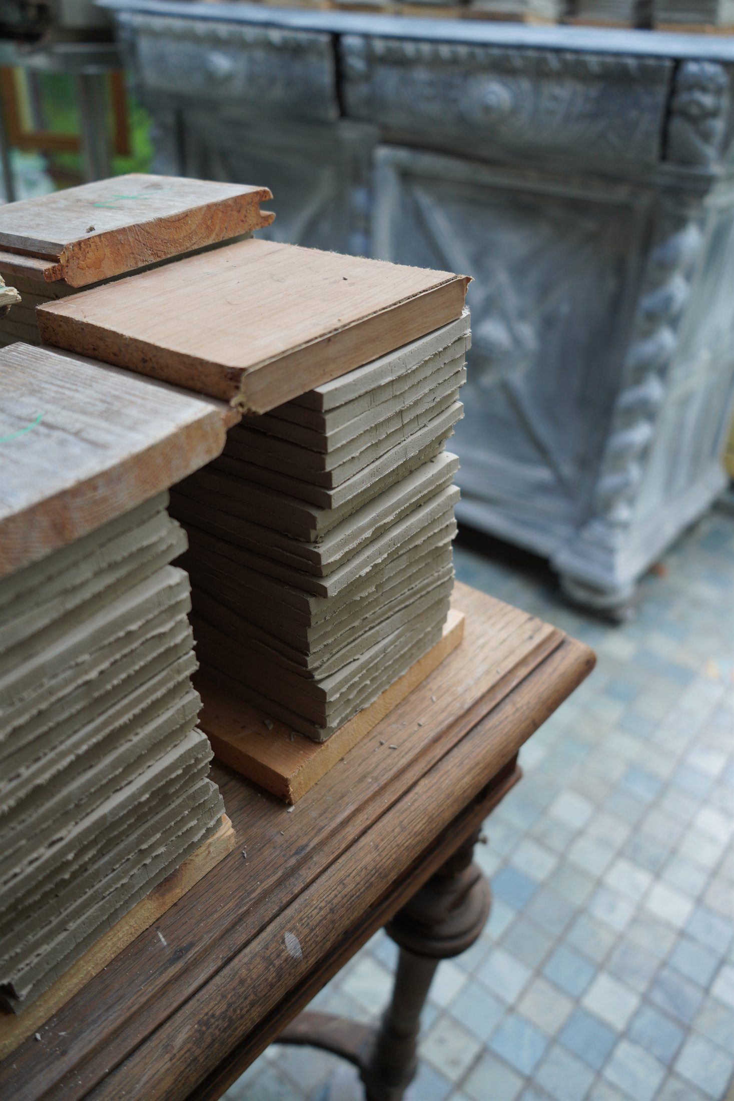 Ruwe handgemaakte tegelstapels die in het atelier onder houten platen tot rust komen.